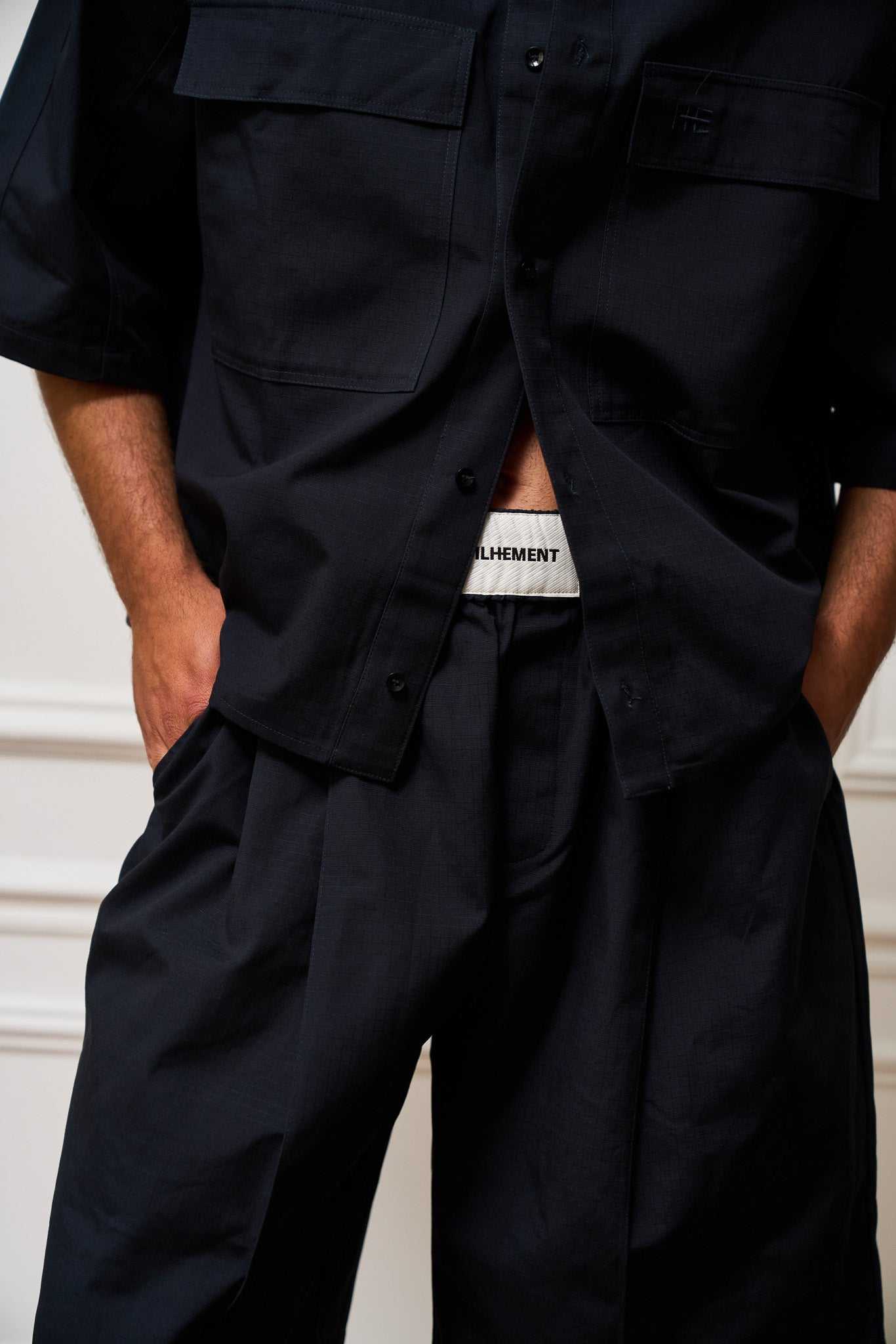 Navy pleated pants made from heavyweight organic ripstop cotton with stitched-down front pleats and tonal embroidery