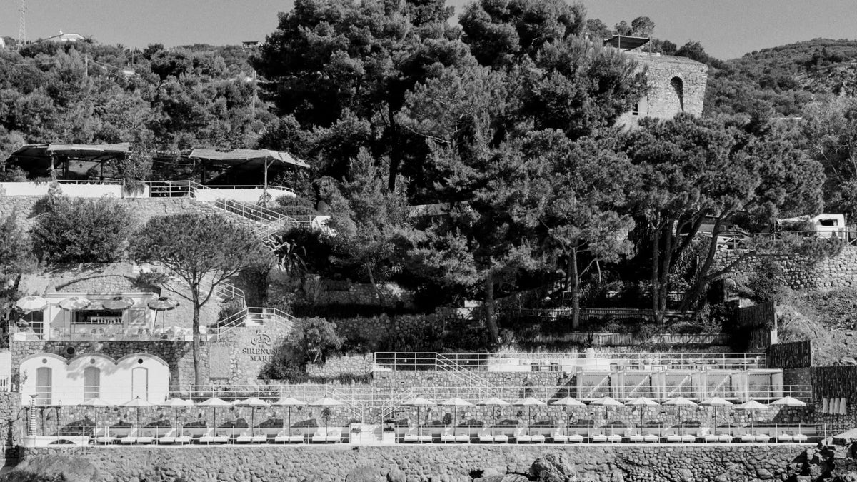 Le Sirenuse Mare viewed from the water, showing its stone terraces, beach level and pine-covered Nerano hillside.