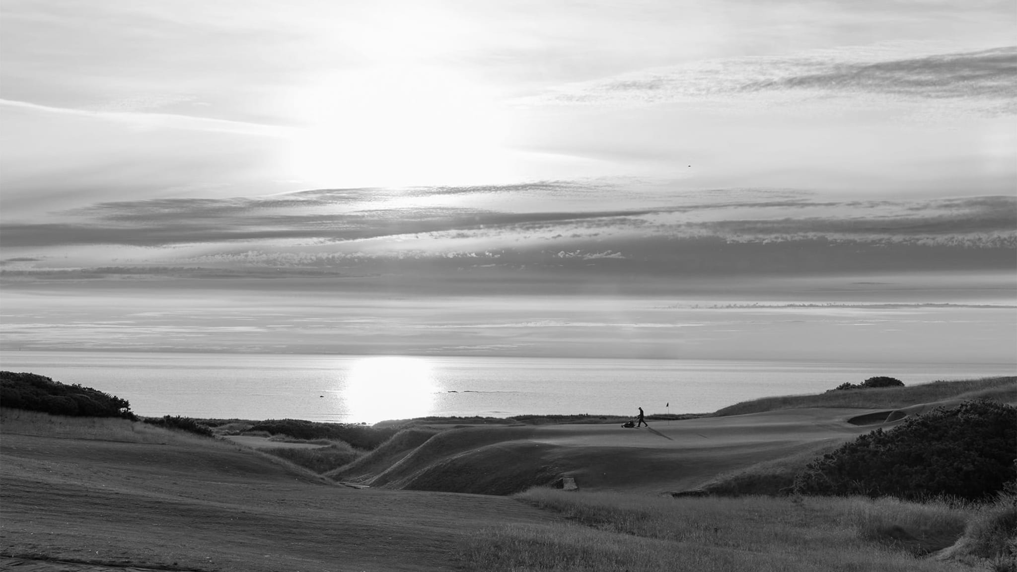 Golfers on the coastal links at St Andrews at sunset, with the North Sea beyond.