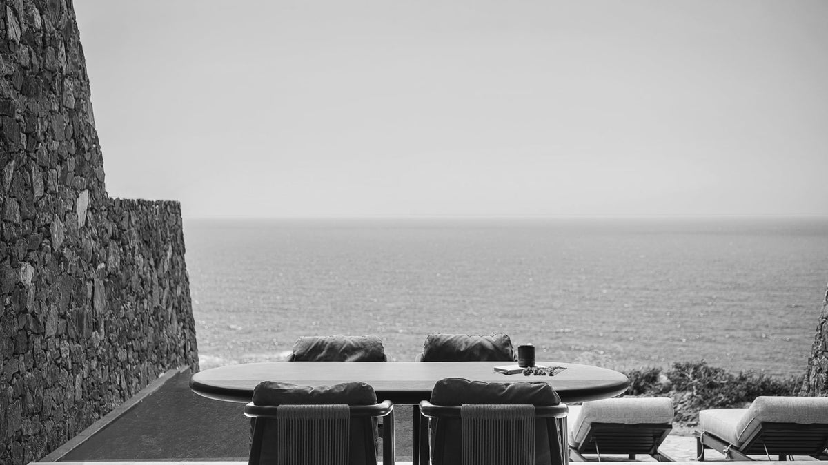 Stone terrace with a dining table and infinity pool overlooking the sea at The Revery in Crete
