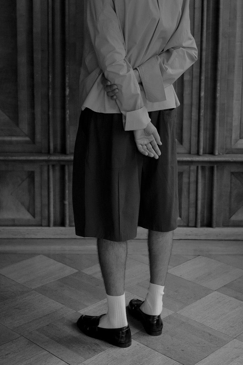 A black and white photograph of a person standing with their back to the camera in a grand, historic room with wooden paneling and a tiled floor.