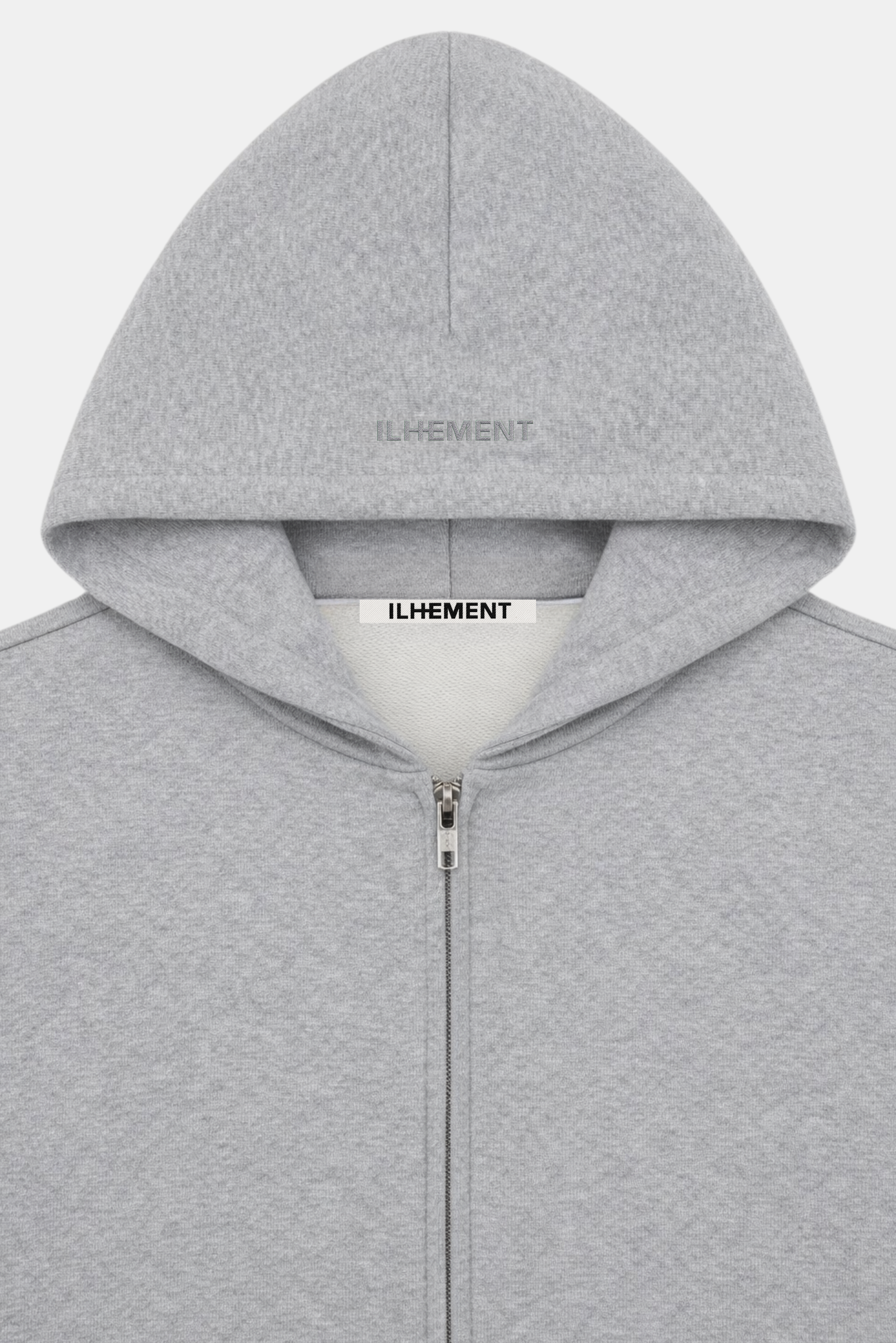 A close-up of a light gray heather zip-up hoodie with the brand name 'ILHEMENT' stitched tonal on the hood and visible on the inner neck label.
